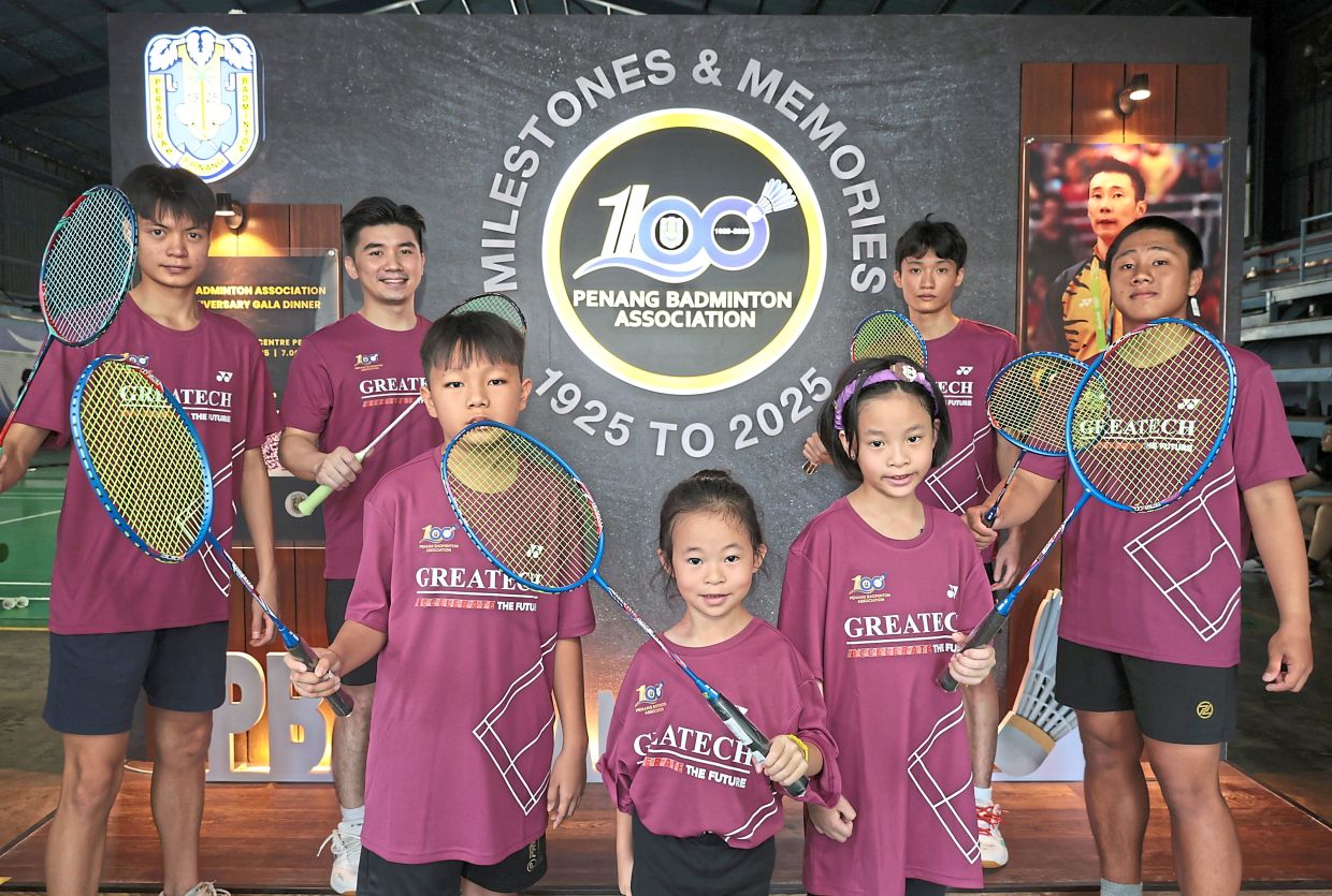 Some players posing in front of the Penang Badminton Association 100th anniversary backdrop at the PBA Badminton Centre in Bukit Dumbar.