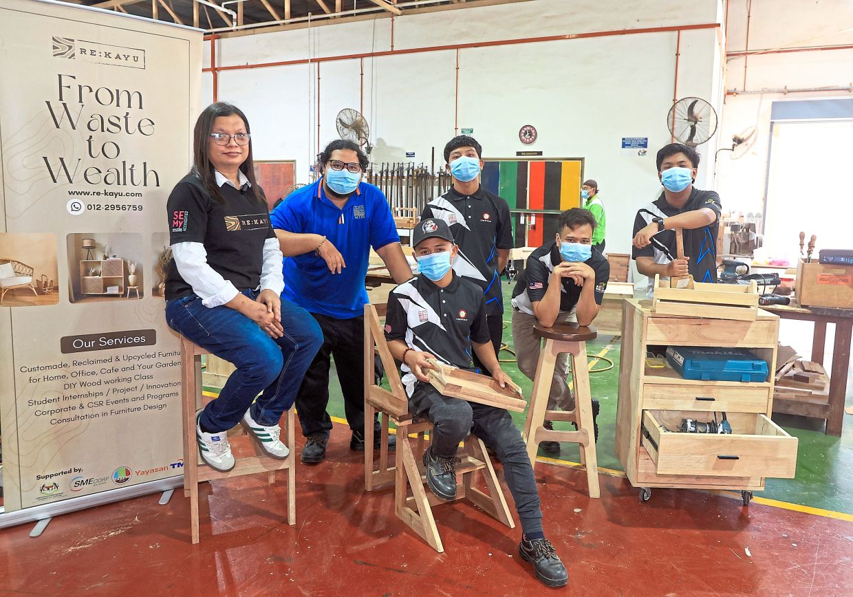 New lease of life: Mohd Faizal (left, seated, without mask) with his trainees and their custom-made recycled wood furniture. — CHAN TAK KONG/The Star