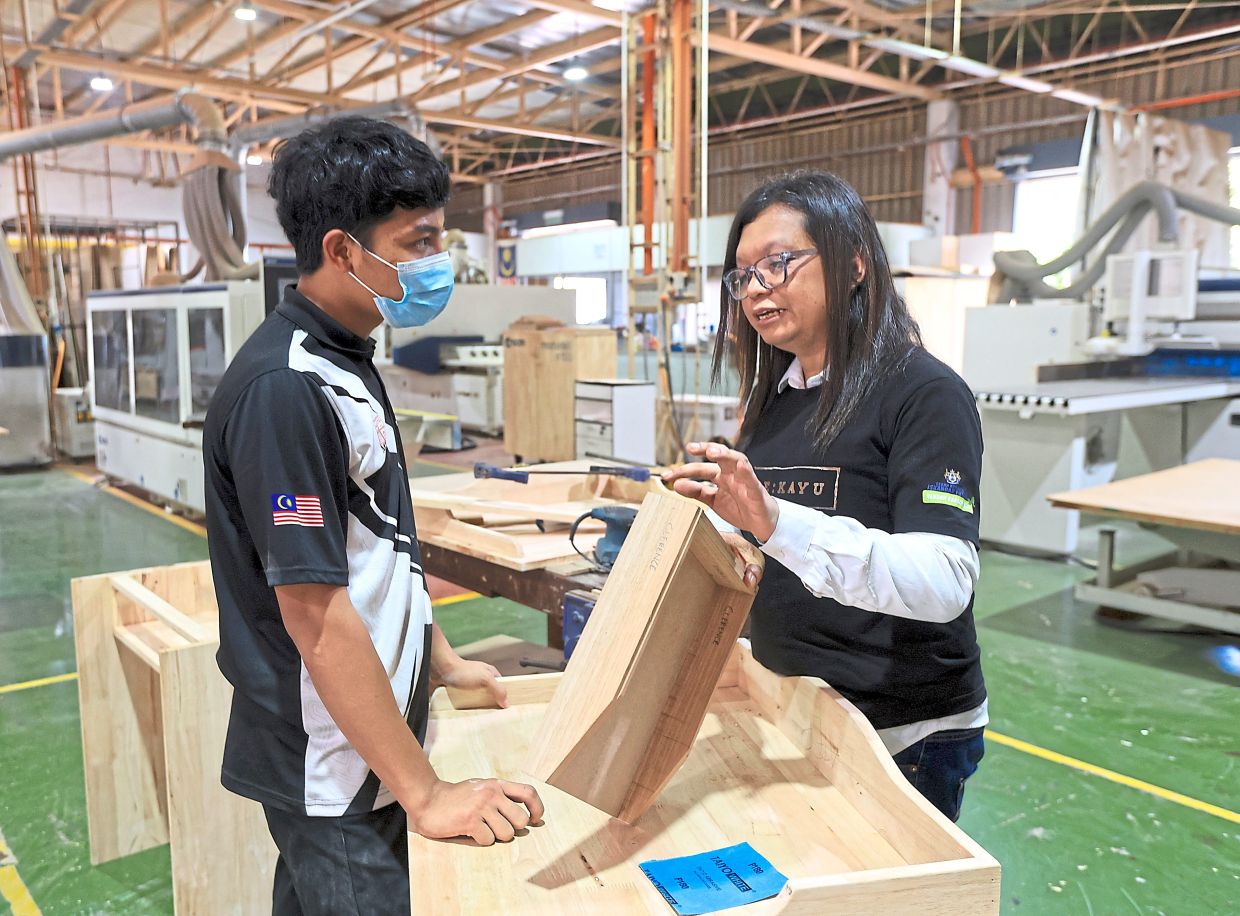 Mohd Faizalguiding one of his trainees in the process of woodworking. — CHAN TAK KONG/The Star