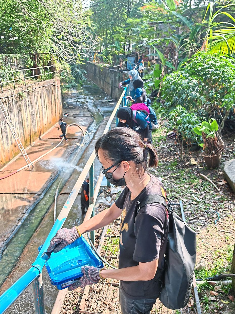 Volunteers painting a monsoon drain railing during the Hari Cuci Malaysia event at PPR Lembah Subang 1.