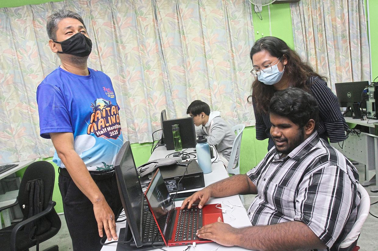 Chew (standing, right) observing trainee S. Puvarasan, 19, build a website as part of his course work at St Nicholas’ Home for the Blind.