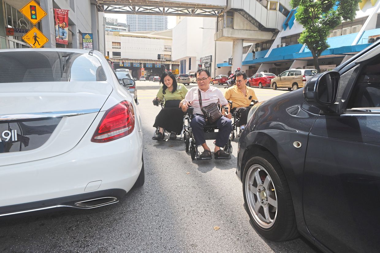 (From left) Teh, Lim and Ooi struggle to access the pavement as they are blocked by double-parked cars in George Town.