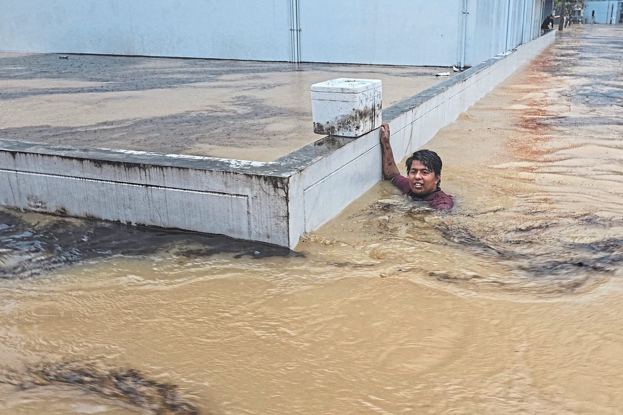 Holding on for dear life: A man clinging to a wall in a flooded street after being swept there while going out to get food supplies in Hat Yai district. — Reuters