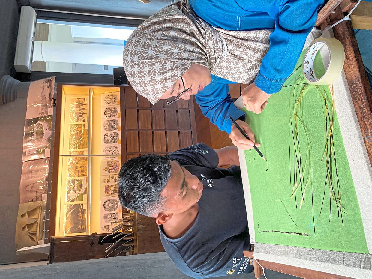 Ros (right) mentoring Amran to ensure the centuries-old craft of keringkam remains.
