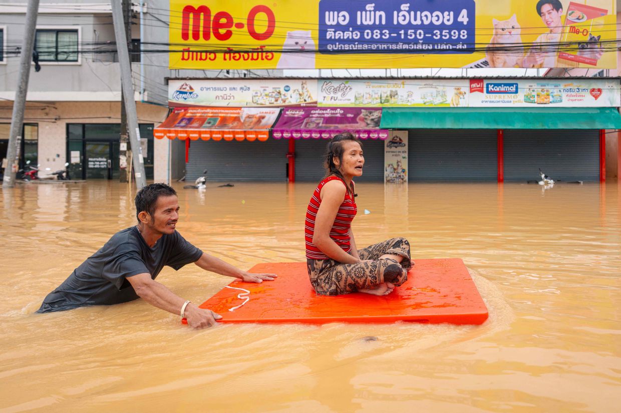A man transporting a woman through flood waters in Hat Yai on Nov 26, 2025. - AFP