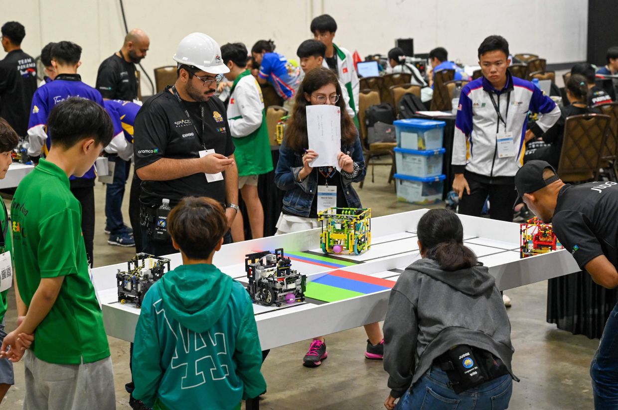 Participants looing on as robots compete during the RoboSports competition at the World Robot Olympiad in Singapore on Nov 27, 2025. - AFP