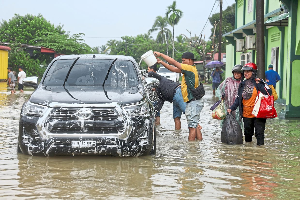 Making good of something bad: A few residents giving their car a wash using the floodwaters in Rantau Panjang, Kelantan. — Bernama