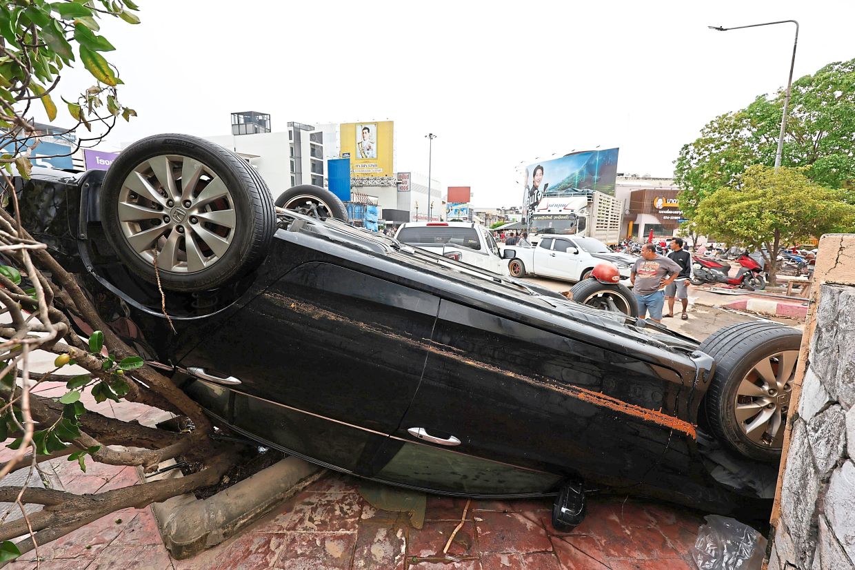 Topsy turvy: A man standing behind a damaged car following floods in Songkhla province, southern Thailand. — AP 