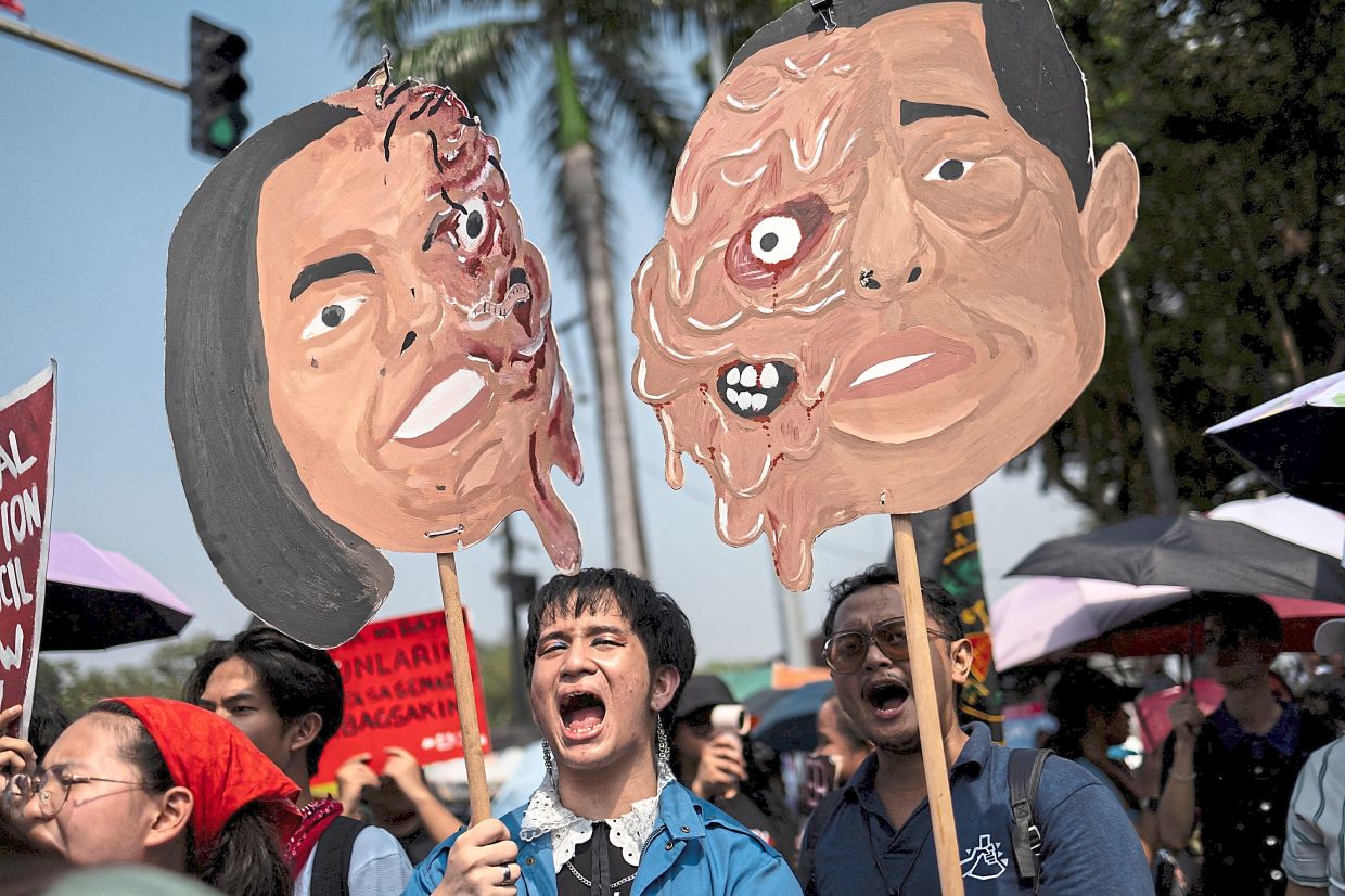 Demonstrators raising props depicting caricatures of Duterte (left) and Marcos.