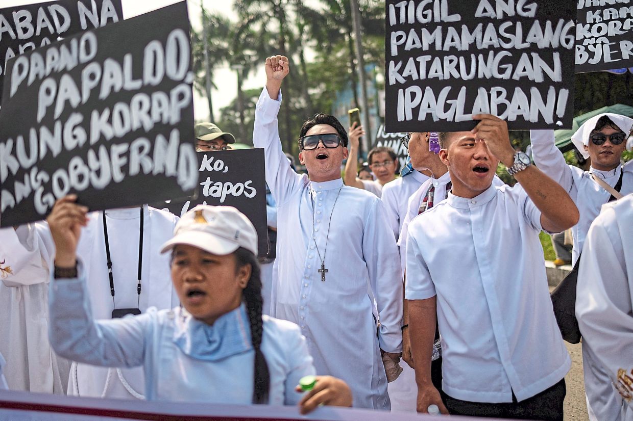 Filipino clergy members shouting as they hold placards during the march.