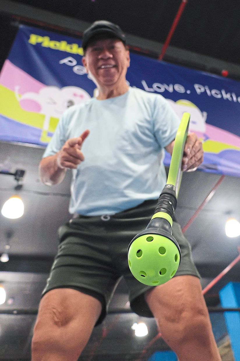 Foo using a suction cup attached to his pickleball paddle handle to retrieve the ball. 