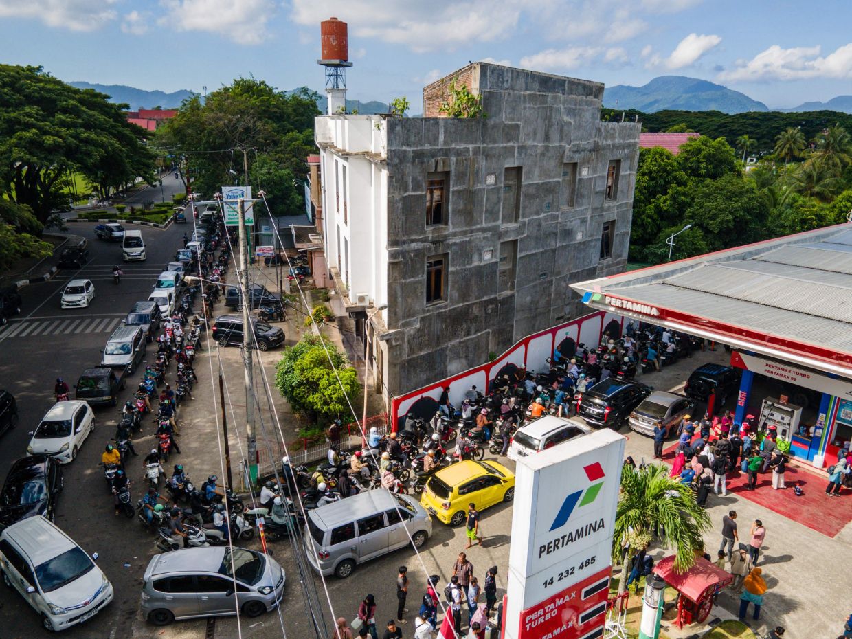Flood-affected residents on foot, motorcyles and cars waiting in long lines at a fuel station in Banda Aceh on Dec 3, 2025. - AFP