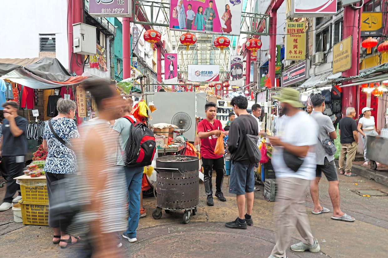 Locals and tourists navigate a maze of stalls brimming with street food and souvenirs in Petaling Street.