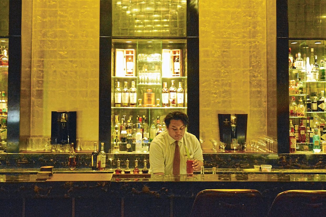 A bartender preparing cocktails at the Astor Bar counter.