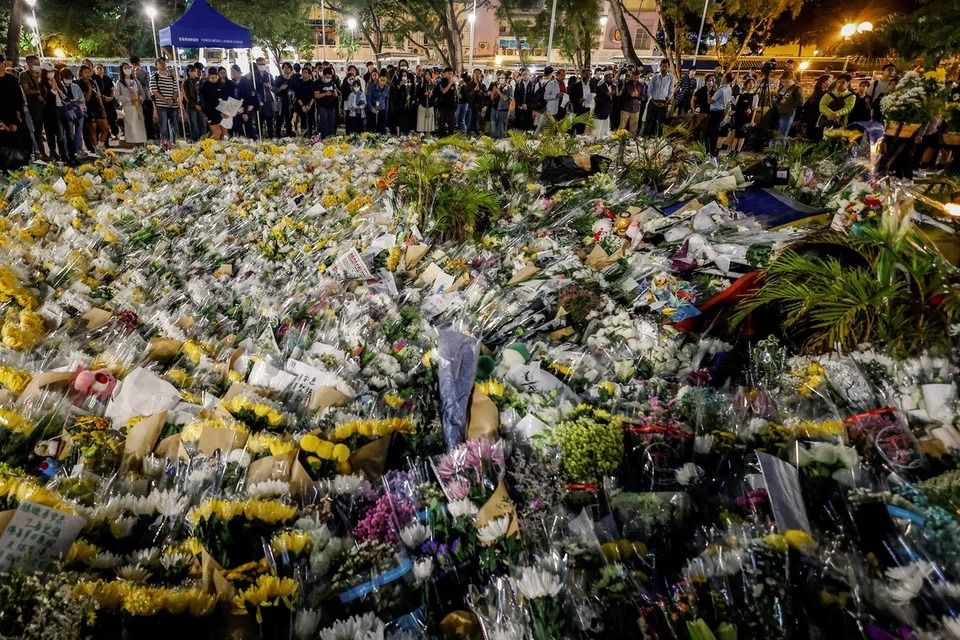 People gather next to a pile of flowers at a makeshift memorial in a small park near Wang Fuk Court on Dec 1. - Photo: Reuters