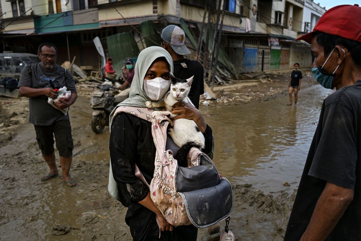 A woman carries her cat on a street still filled with mud after a flash flood hit the area in Aceh Tamiang, Aceh province, on Saturday, December 6, 2025. -- Photo by YT HARIONO / AFP