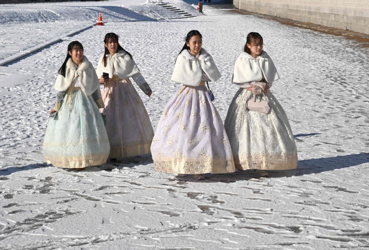 Visitors wearing traditional hanbok dresses walk on the snow-covered grounds of Gyeongbokgung Palace in Seoul on December 5, 2025, after the season's first snowfall. -- Photo by Jung Yeon-je / AFP