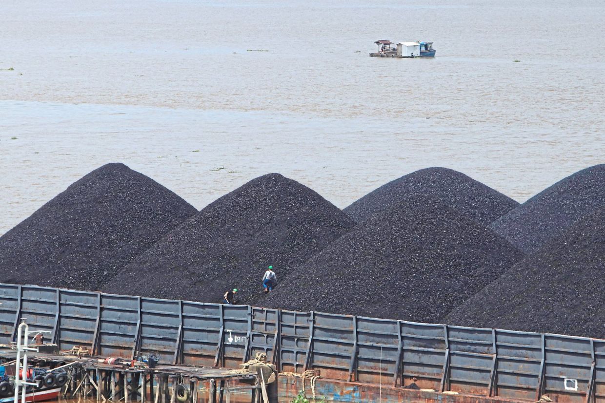 Workers are seen on a pile of coal transported on a barge in Samarinda, East Kalimantan, in 2022. The report by Singapore researchers found that those from lower income groups in the region were more hesitant about carbon taxes as they worry about higher energy prices. — AFP