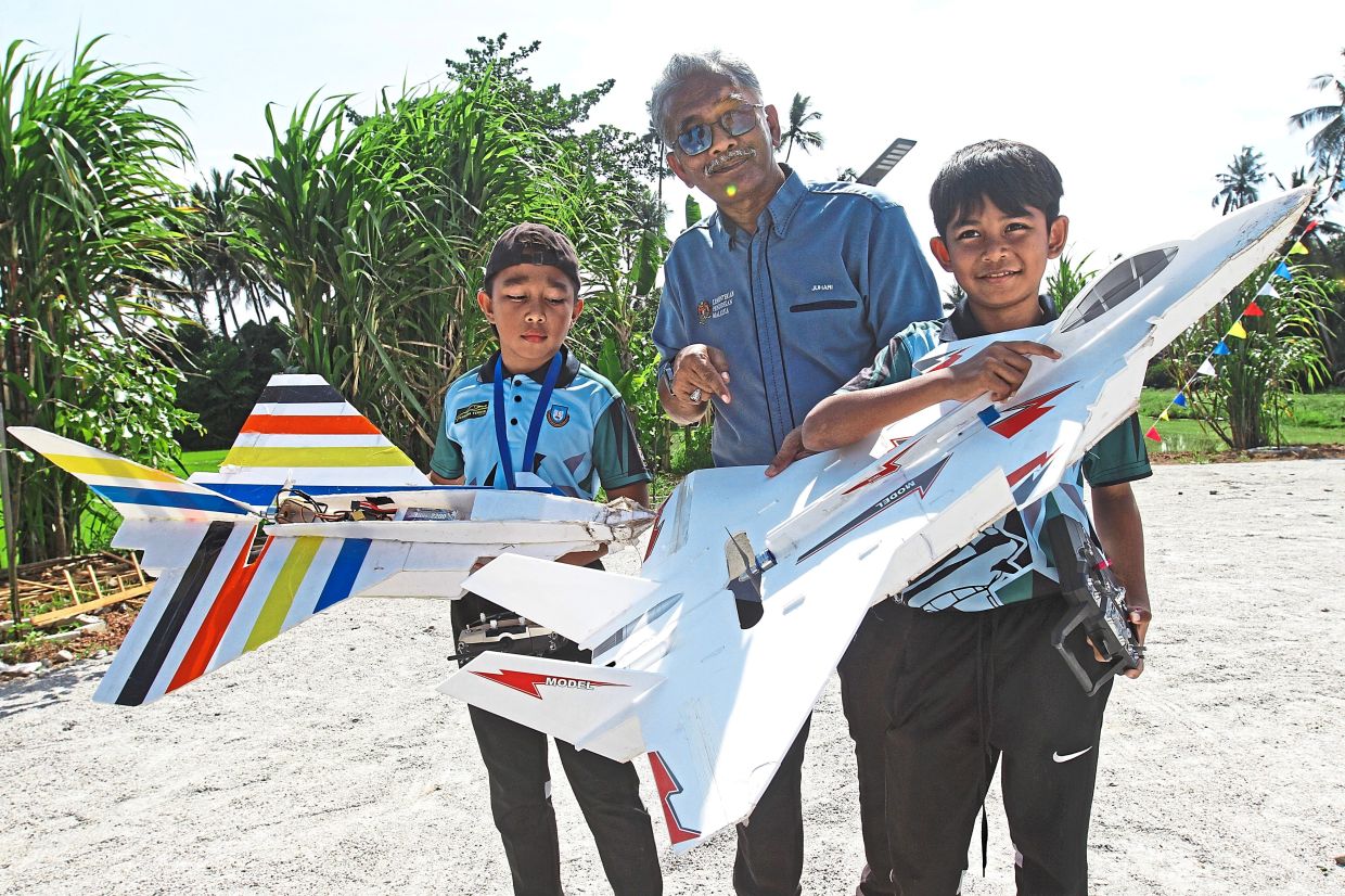 School headmaster Juhari Jusoh (centre) with Muhamad Darwish Izzairil Zakaria (right) and Umar Hadi Mohd Rozhan, both 11, showing their RC jets at the event. 