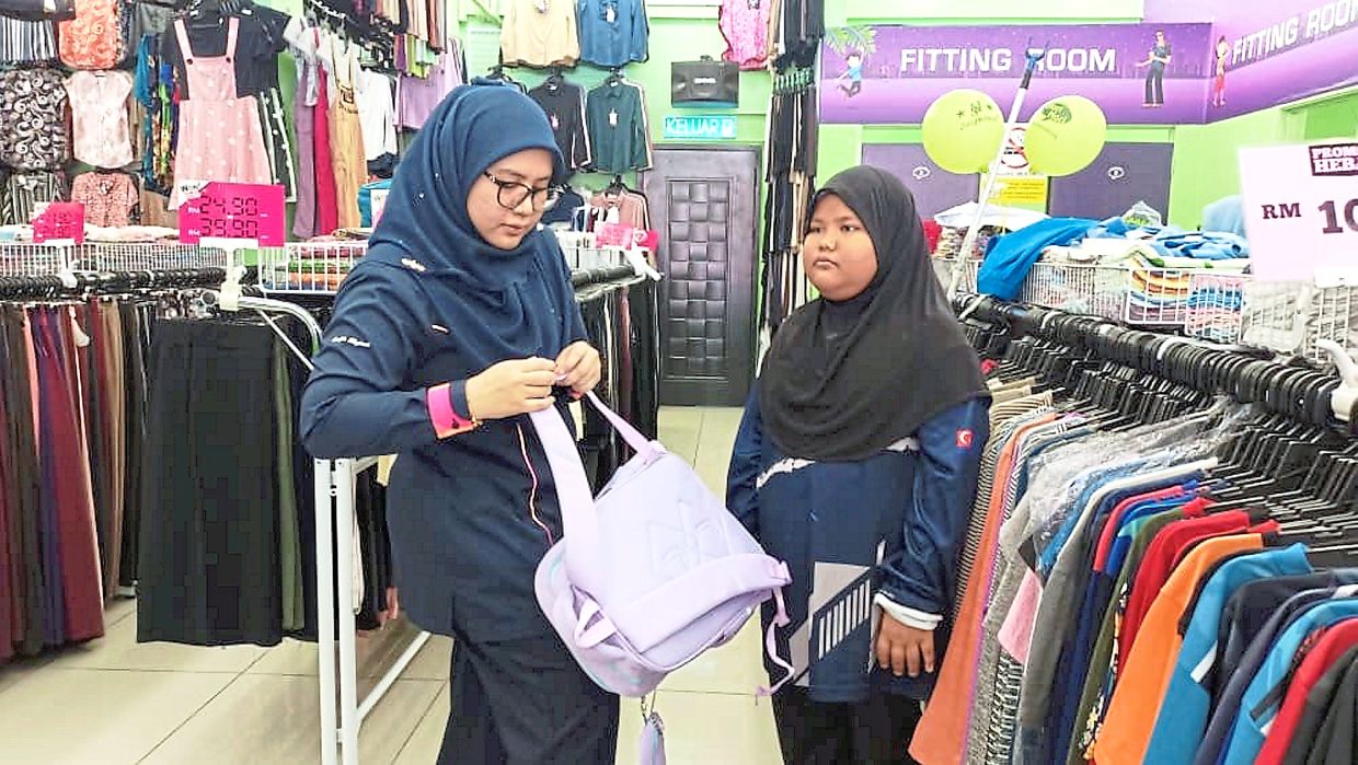 Yayasan JCorp staff Sharifah Hashimah Syed Mohd Nazar (left) helping one of the 16 SK Pulau Sibu pupils buy school supplies at a supermarket in Mersing.