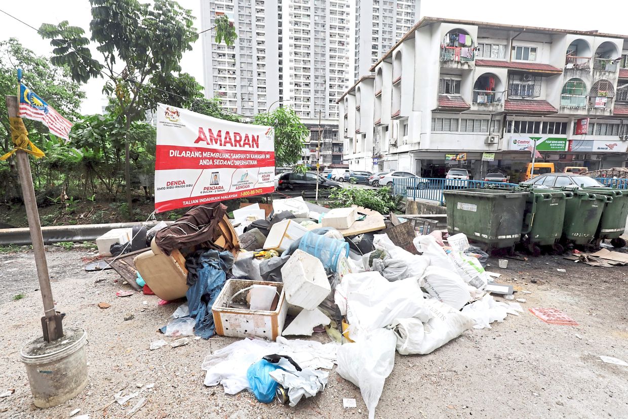A banner warning against throwing rubbish does not seem to be educating people in United Garden, KL as waste is left outside the bins.