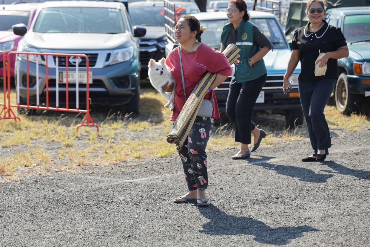 A woman carrying a dog and a mat as she evacuates to a shelter, following fresh military clashes between Thailand and Cambodia along parts of their disputed border, in Buriram province on Dec 8, 2025. - Reuters