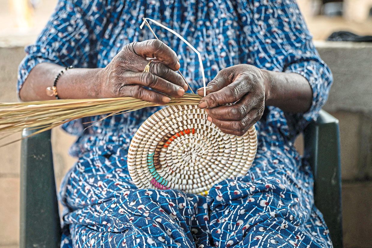 A woman weaves a colorful Senegalese handicraft basket in Mborine, on November 12, 2025. While the women of Mborine village rarely leave this corner of Senegal, their popular creations travel in much wider circles, having become trendy in places like the United States or France.Flip over the price tag on a Senegalese-style basket in a Western box store, however, and there is a high chance it was made in Vietnam, a large exporter of knockoffs. Meanwhile, the price for authentic handmade Senegalese baskets can be astronomical abroad, with little of the markup going to the weavers. While a large laundry-style basket might sell for 13,000 CFA francs ($23) at a market after passing through a middleman, those exported abroad go for well over $150. (Photo by NICOLAS REMENE / AFP)