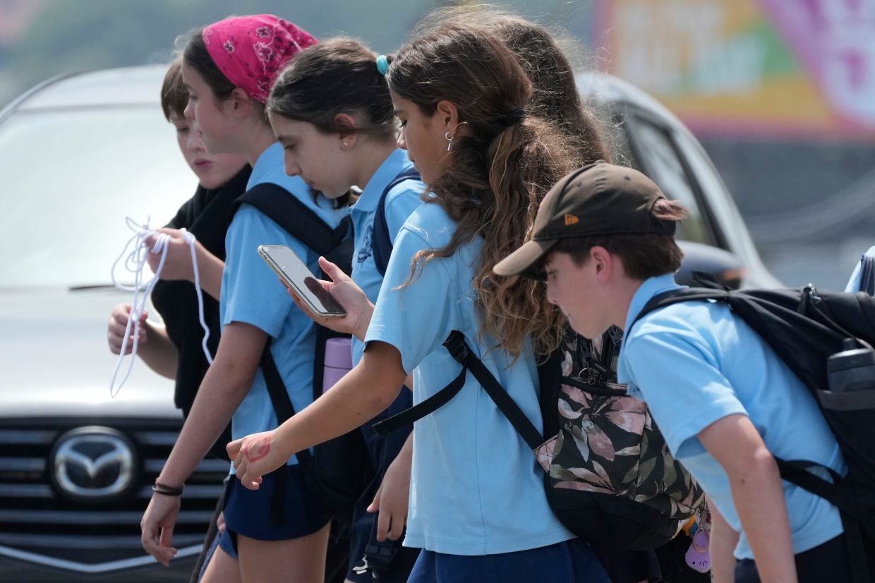 A school girl uses her phone as she walks with a group of kids in Sydney on Dec 8, 2025. — AP