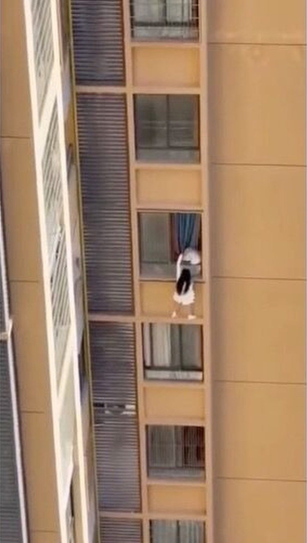 The woman is seen perched on a wall high up on the building while holding onto a curtain. Photo: ettoday.net