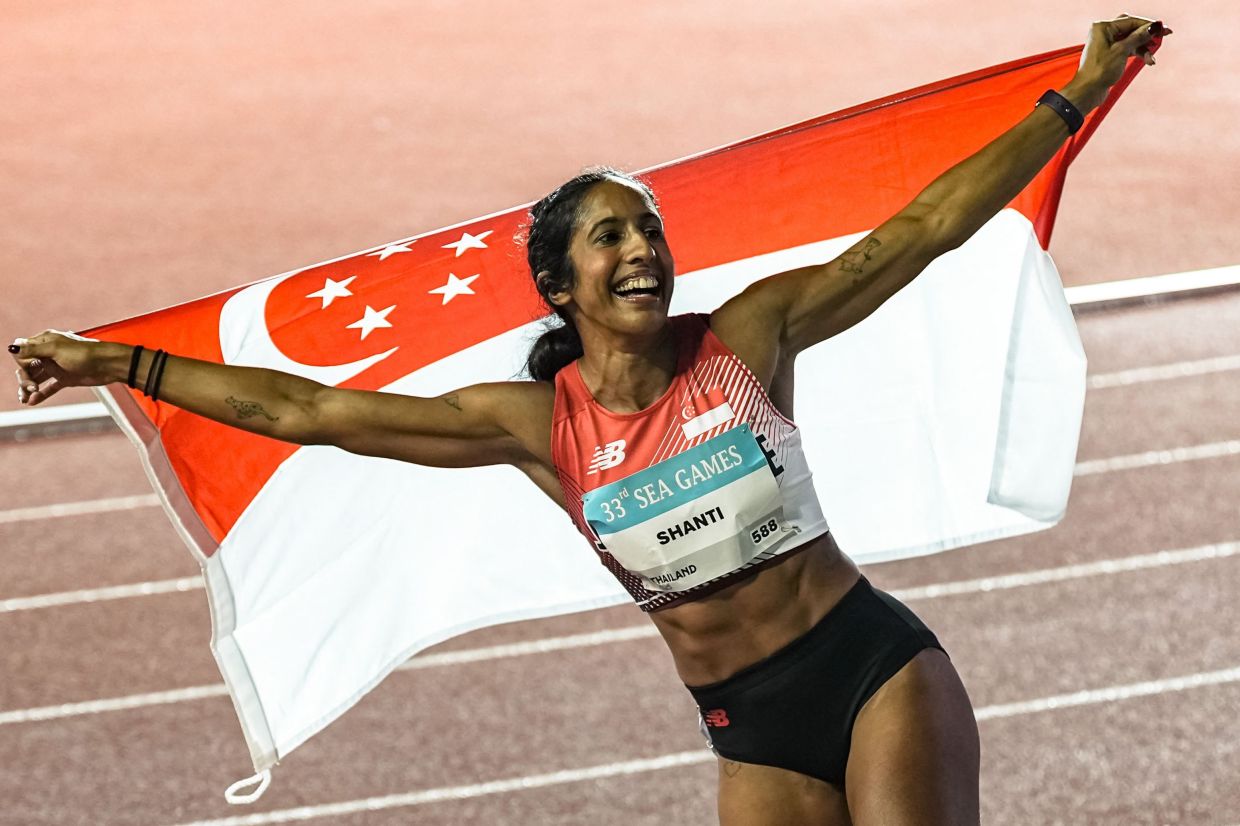 Singapore's Shanti Pereira celebrates with the Singapore national flag after winning the women's 100m final of the athletics event during the 33rd Southeast Asian Games (SEA Games) at the Suphachalasai National Stadium in Bangkok on December 11, 2025. (Photo by Chanakarn Laosarakham/ AFP)