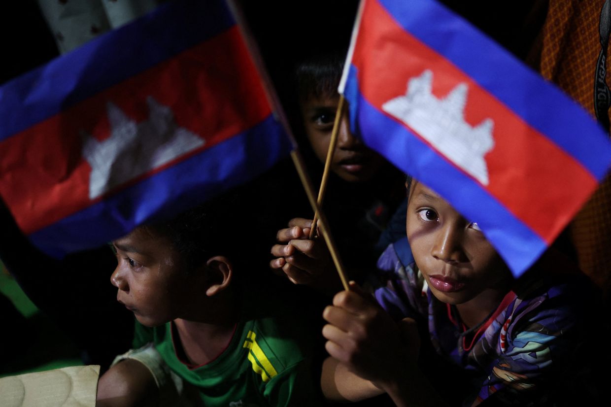 Boys hold Cambodia national flags as they wait to receive supplies at a refugee camp, amid clashes between Thailand and Cambodia along a disputed border area, in Srei Snam, Siem Reap Province, Cambodia, Friday, December 12, 2025. -- Photo: REUTERS/Kim Hong-Ji