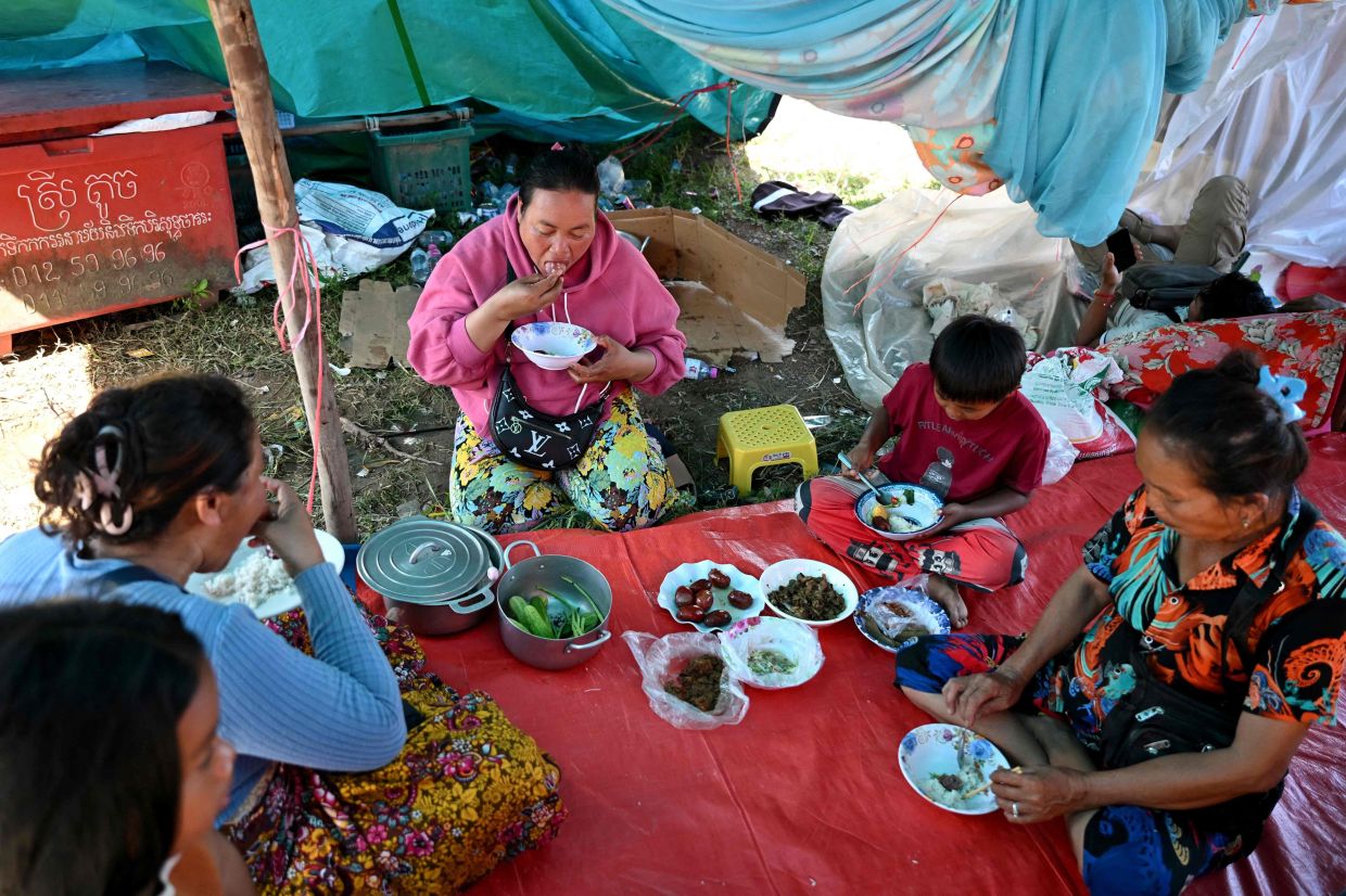Former migrant worker Cheav Sokun (centre) eating a meal with family at a temporary camp for displaced people set up at a former market in Banteay Meanchey province on Dec 13, 2025. - AFP