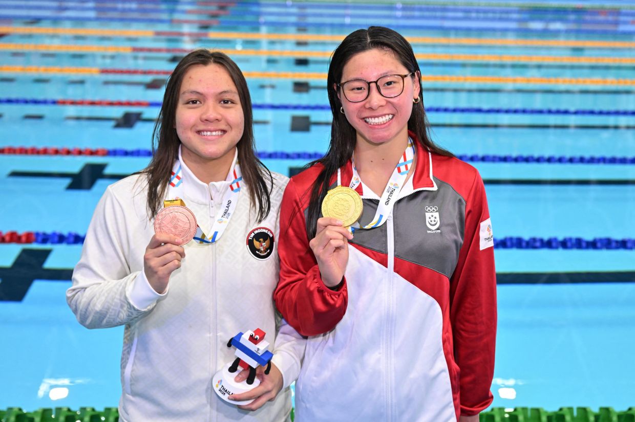 Southeast Asian Games - SEA - Swimming - SAT Swimming Pool, Bangkok, Thailand - Sunday, December 14, 2025. Gold medallist Singapore's Letitia Sim celebrates during the women's 200m breaststroke medal ceremony with bronze medallist Indonesia's Adellia. Photo: REUTERS/Andy Chua