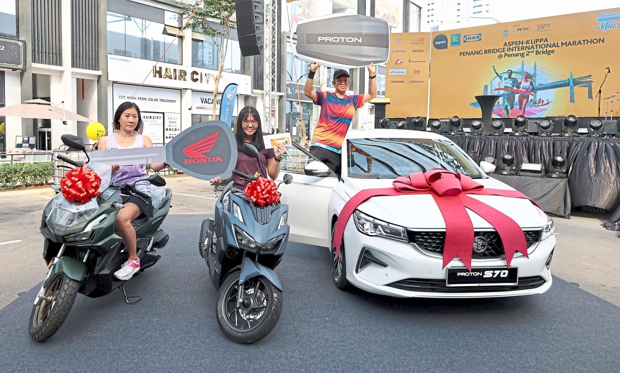 Cause for celebration: (From left) Penangite Ooi Chew Hoon, 50; Kedah resident Tan Xin Rou, 28; and engineer Cham Chiong Fook, 43, showing the scooters and Proton S70 that they won in the lucky draw at the Aspen-Klippa Penang Bridge International Marathon 2025 in Batu Kawan.