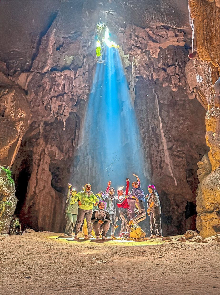 A shaft of sunlight lights up the main chamber of Gua Ikan as a caving group poses for a photo.