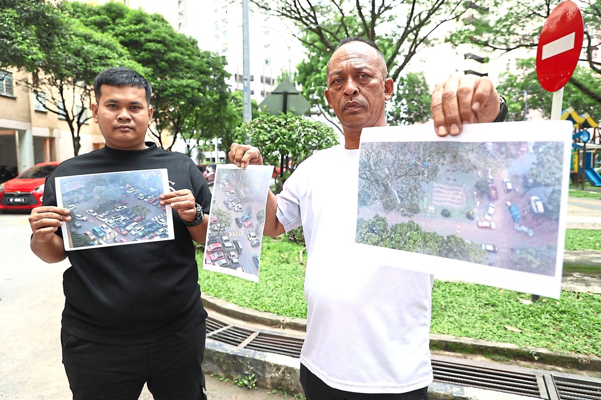 PPR Kg Muhibbah residents Shahrul Azwan Zainal Abidin (left) and Yop Affendi Darus holding up photos of flooding at the open-air carpark.