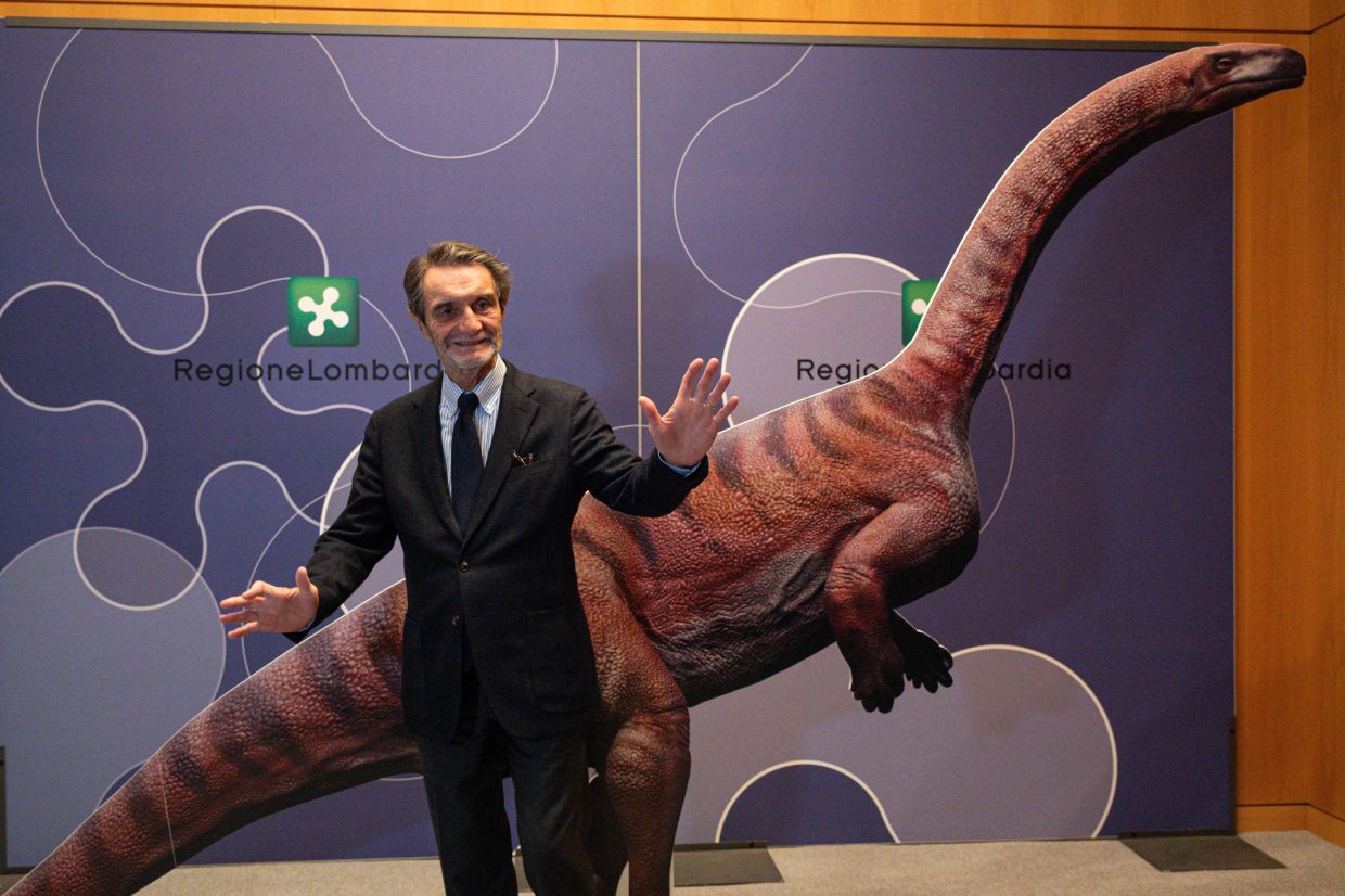 Attilio Fontana, President of Lombardia Region, poses for a photograph with a cardboard dinosaur during a press conference to present the discovery of thousands of dinosaur tracks discovered in Italy's Stelvio National Park. — Photo by Piero CRUCIATTI / AFP