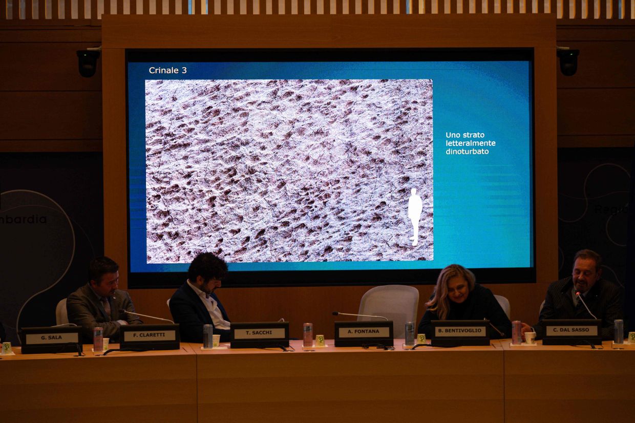Paleontologist at the Natural History Museum of Milan Cristiano Dal Sasso (R) comments on photos on a screen during a press conference to present the discovery of thousands of dinosaur tracks discovered in Italy's Stelvio National Park. – Photo: CRUCIATTI / AFP)