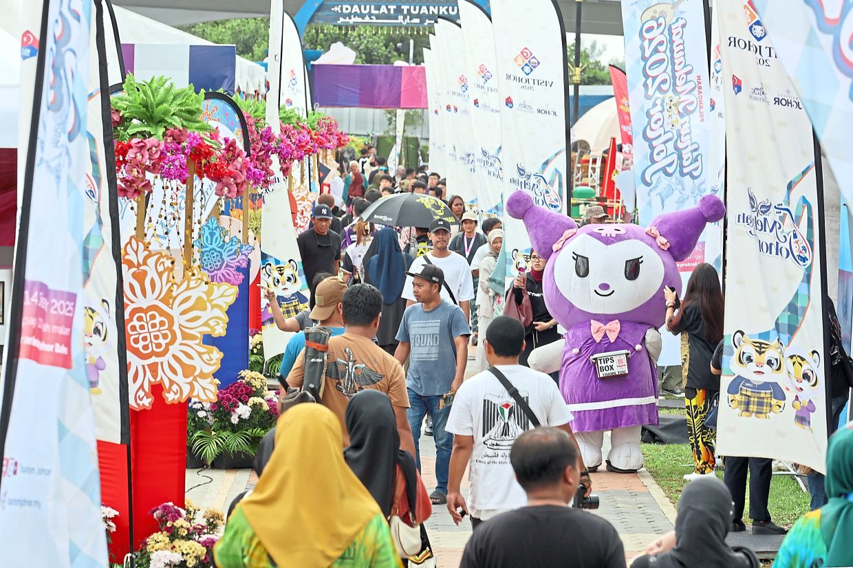 Visitors milling around Malaysia Cultural Festival 2025 and posing with a durian mascot (below), a feature of a booth highlighting the Segamat district.