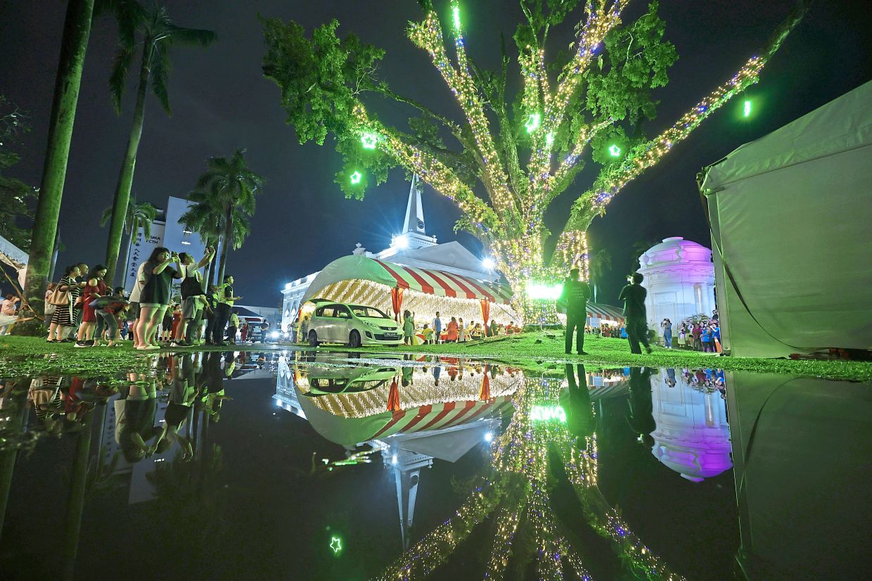 The church and its illuminated mahogany tree beautifully reflected on the surface of a water puddle after rain. 