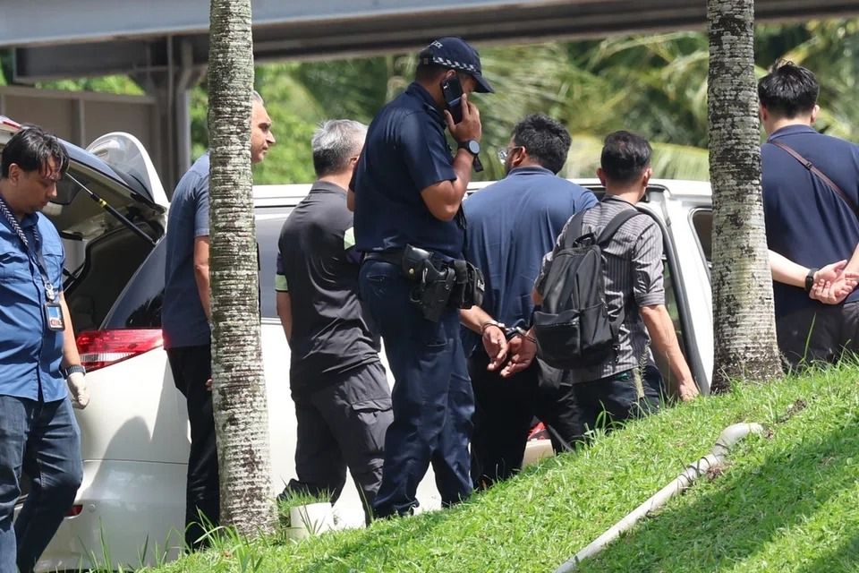 At about 1.45pm, a handcuffed man wearing a blue top was led to a white car by police officers. -- PHOTO: LIANHE ZAOBAO