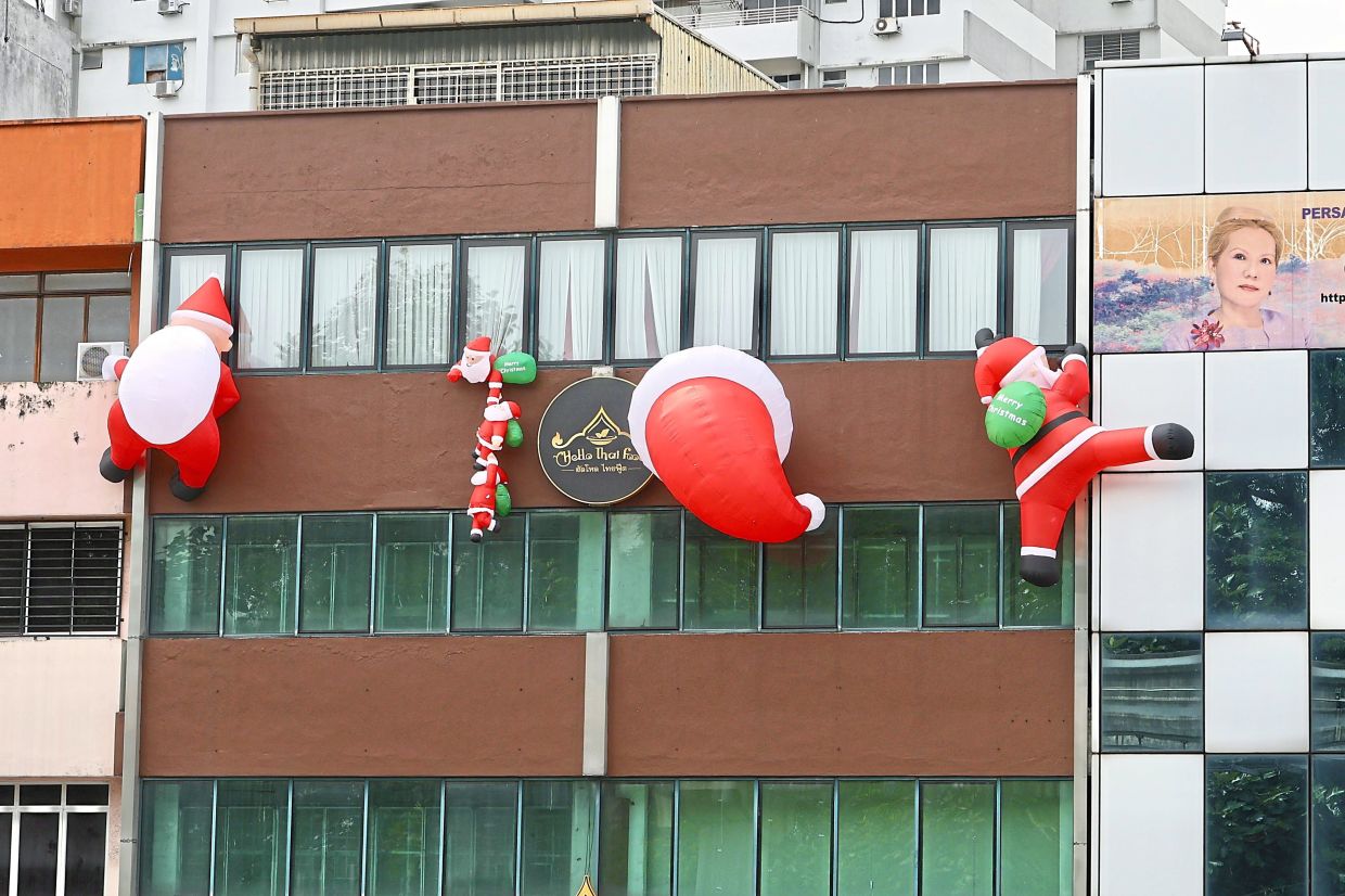 A cheeky display of Santa Claus scaling the wall and climbing into windows of a building in Kuala Lumpur.