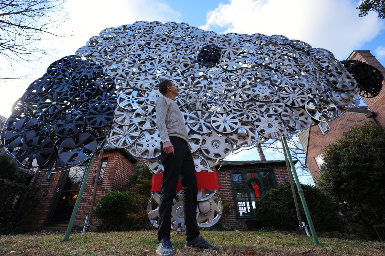 Cyclist Barnaby Wickham poses for a portrait in front of his art structure made from hubcaps, Thursday, Dec. 11, 2025, at his home in Baltimore. (AP Photo/Stephanie Scarbrough)