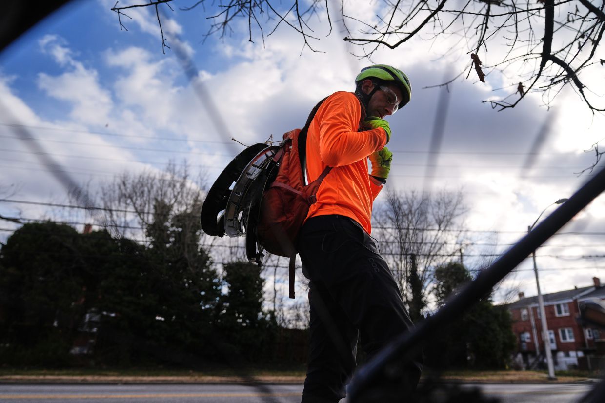 Cyclist Barnaby Wickham fastens lost hubcaps to his backpack to transport them to his home, Thursday, Dec. 11, 2025, in Baltimore. (AP Photo/Stephanie Scarbrough)