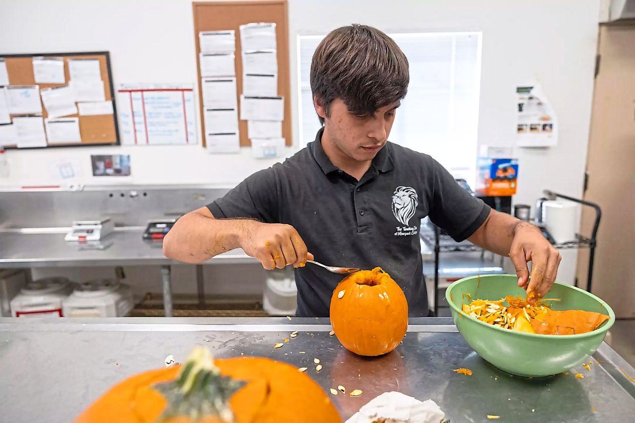 Student Sebastian Villa scoops seeds out of a pumpkin for animal meal prep.