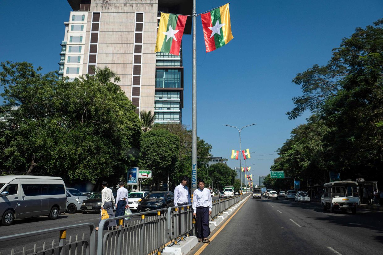 Pedestrians waiting to cross a road under national flags displayed ahead of Myanmar's general election in Yangon on Dec 23, 2025. Myanmar junta has touted polls starting Dec 28 as a path to peace, but the vote will be blocked from rebel-held enclaves and monitors are dismissing it as a ploy to disguise continuing military rule.- AFP