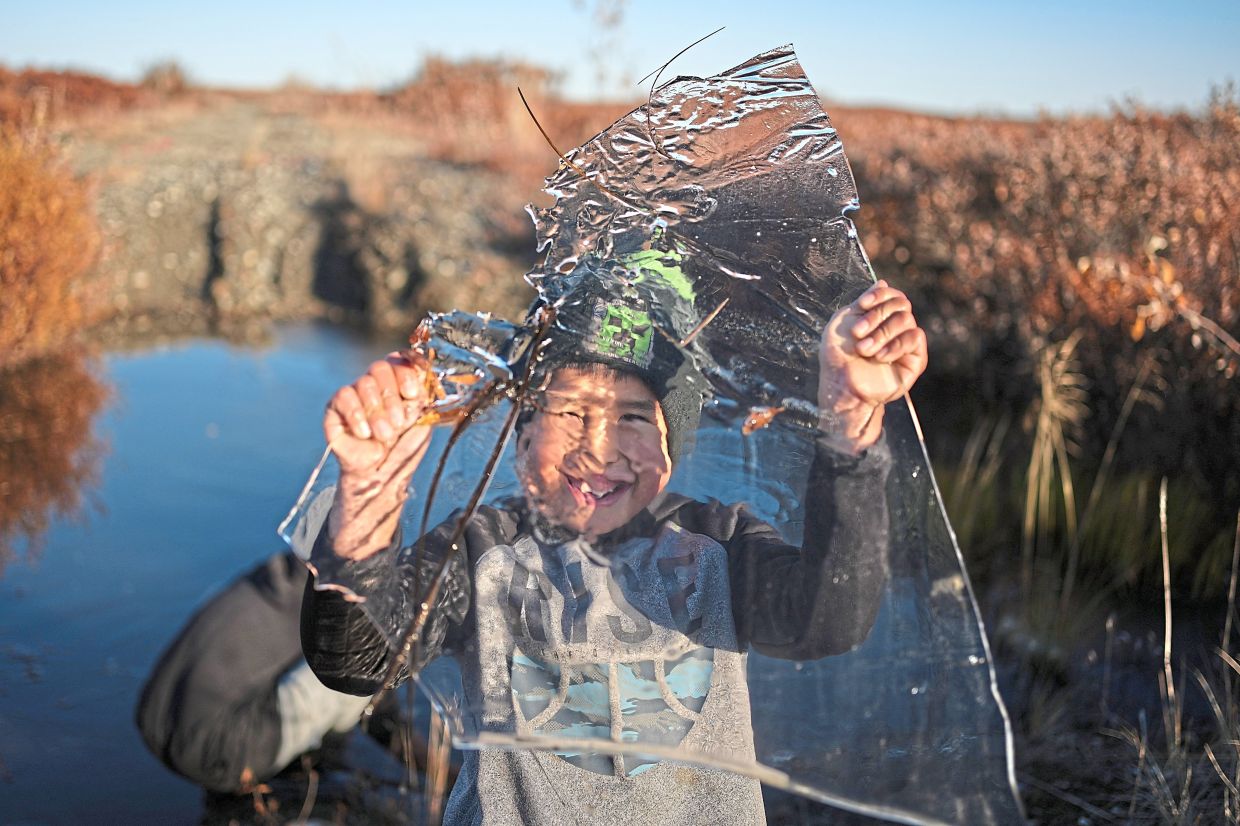 James playing with a slab of ice taken from a pond that formed on a warped road caused by thawing permafrost in Kotzebue, Alaska. — Photos: AP