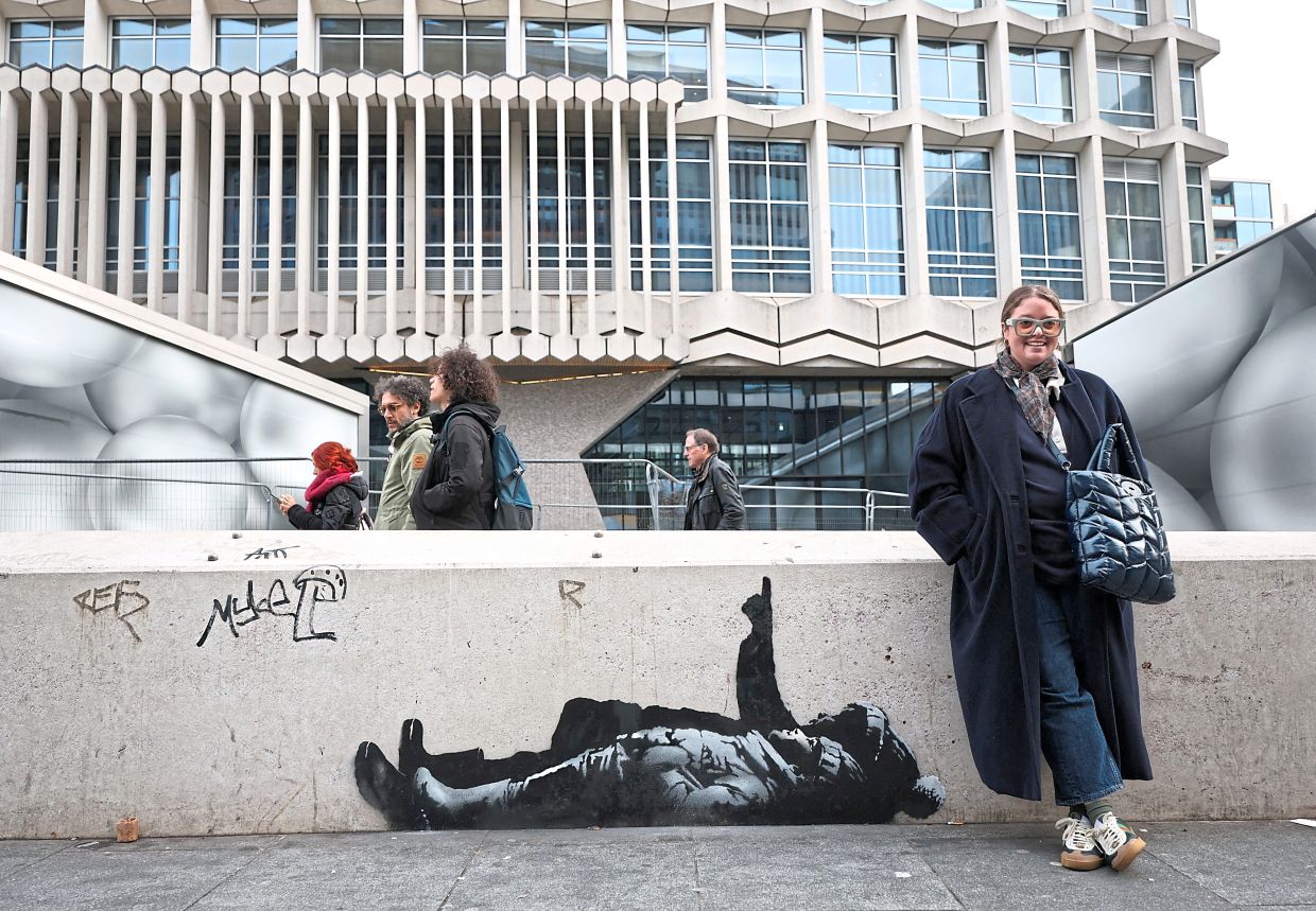 A person stands beside a new mural reported to be by anonymous artist Banksy, in Tottenham Court Road, London, Britain, December 22, 2025. REUTERS/Isabel Infantes