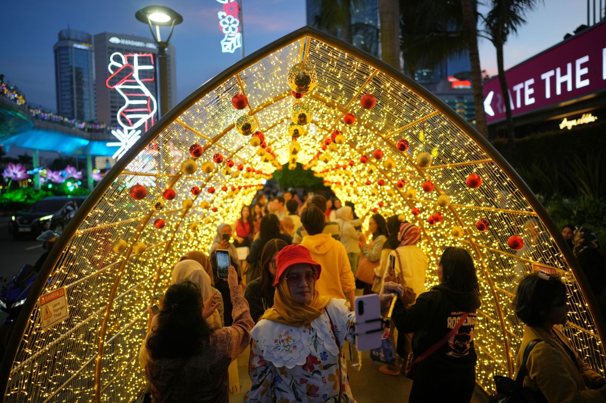 People walk under a Christmas light display in Jakarta, Indonesia, Wednesday, Dec. 24, 2025. -- AP Photo/Dita Alangkara