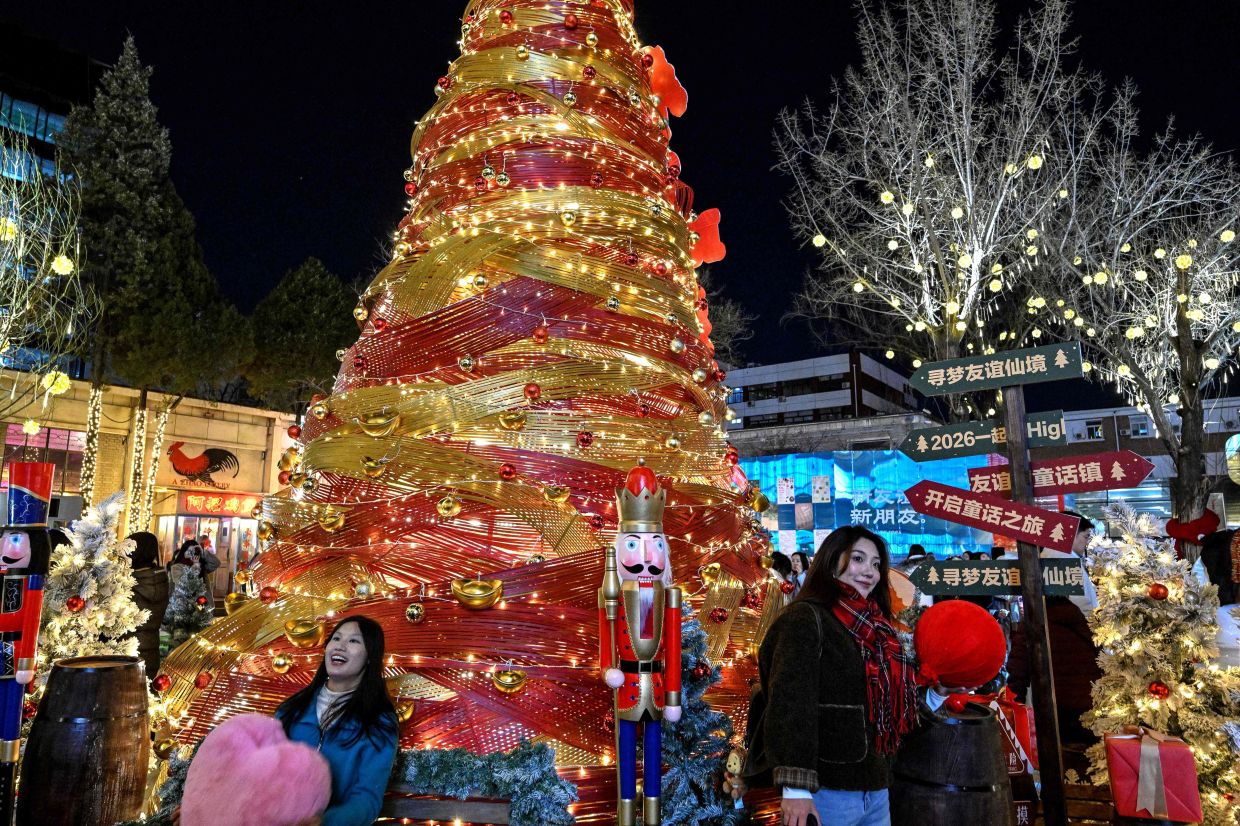 People pose next to an illuminated Christmas tree at a park in Beijing on Thursday, December 25, 2025. -- Photo by Adek BERRY / AFP